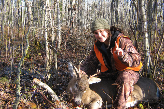 Young woman posing with a White-Tailed Deer that she has just shot.