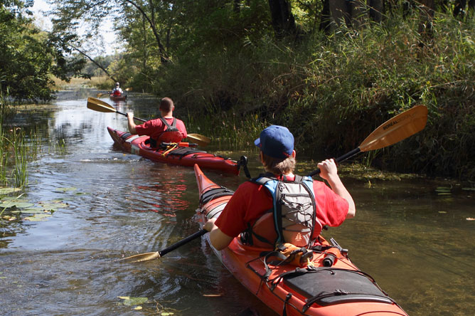  Three young kayakers who use a very narrow channel overgrown with plants.