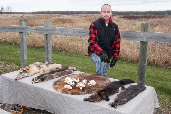 Man standing behind a table where various pelts are displayed.