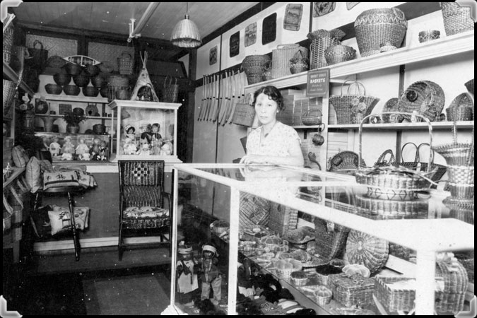 A woman at the counter of a store well-stocked with baskets; taken in the 1930s