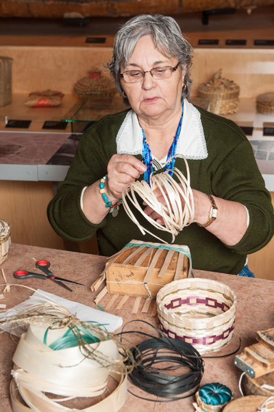 Une femme assise derrière une table et confectionnant un panier.