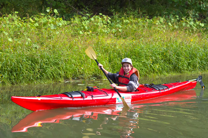 Un jeune homme en kayak rouge dans un chenal vu de côté