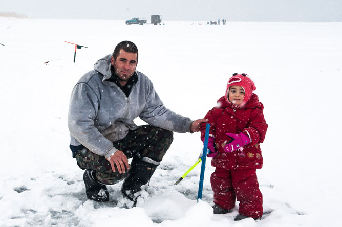 Fillette avec son père faisant de la pêche sur la glace.
