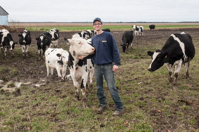 Un jeune agriculteur avec plusieurs vaches noires et blanches dans un champ
