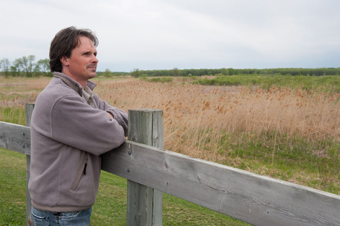 Le biologiste Philippe Brodeur appuyé sur une clôture de bois devant le marais permanent
