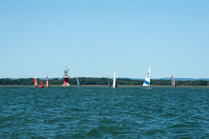 Colourful sailboards on Lake Saint-Pierre, near a red buoy and lighthouse